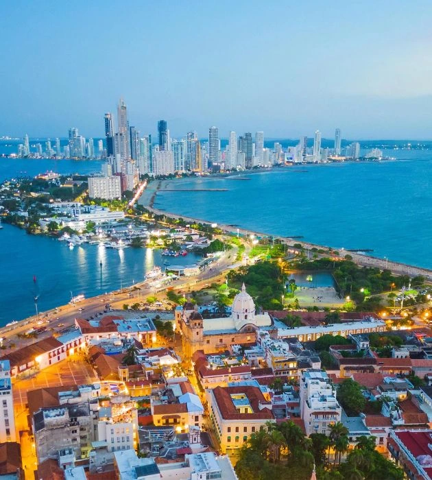 Vista aérea de Cartagena de Indias al atardecer con el centro histórico y Bocagrande iluminados.