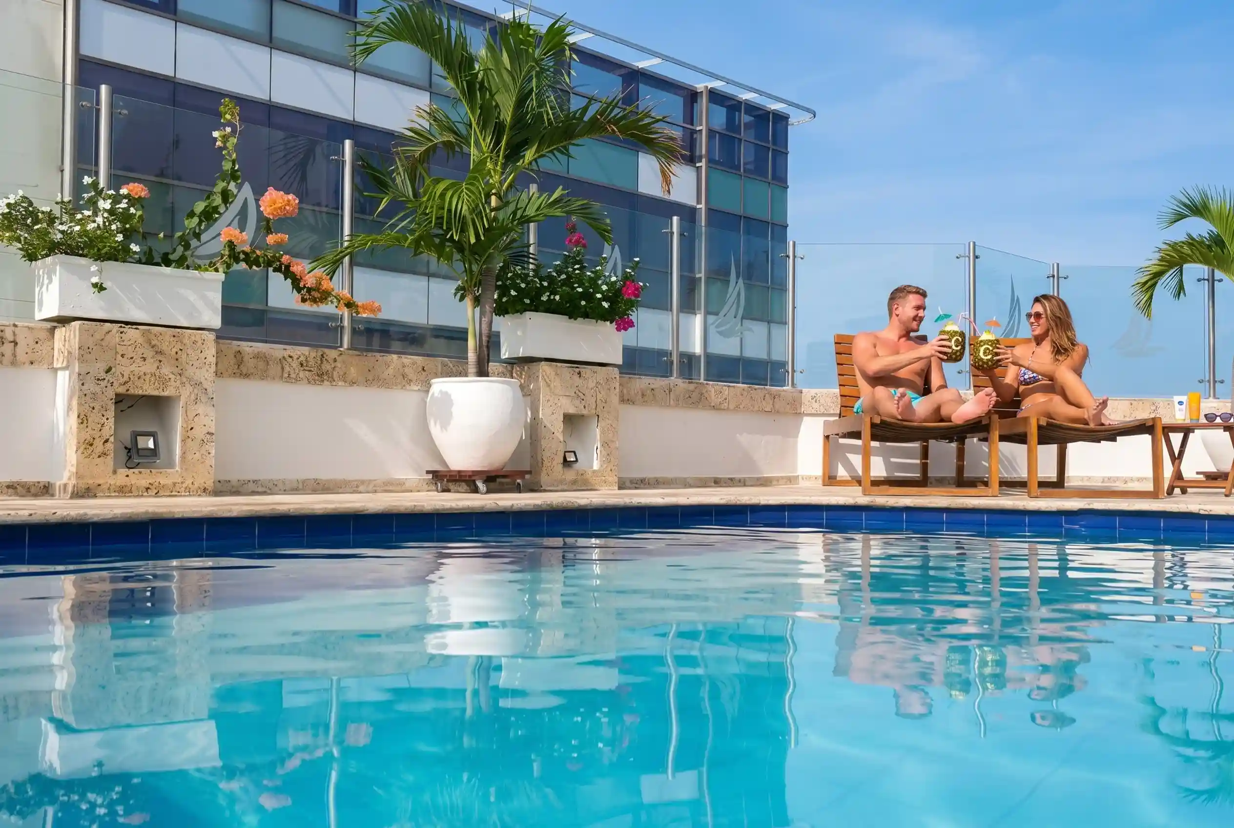 Pareja brindando con bebidas tropicales mientras descansa en asoleadoras junto a la piscina de un hotel en Cartagena.