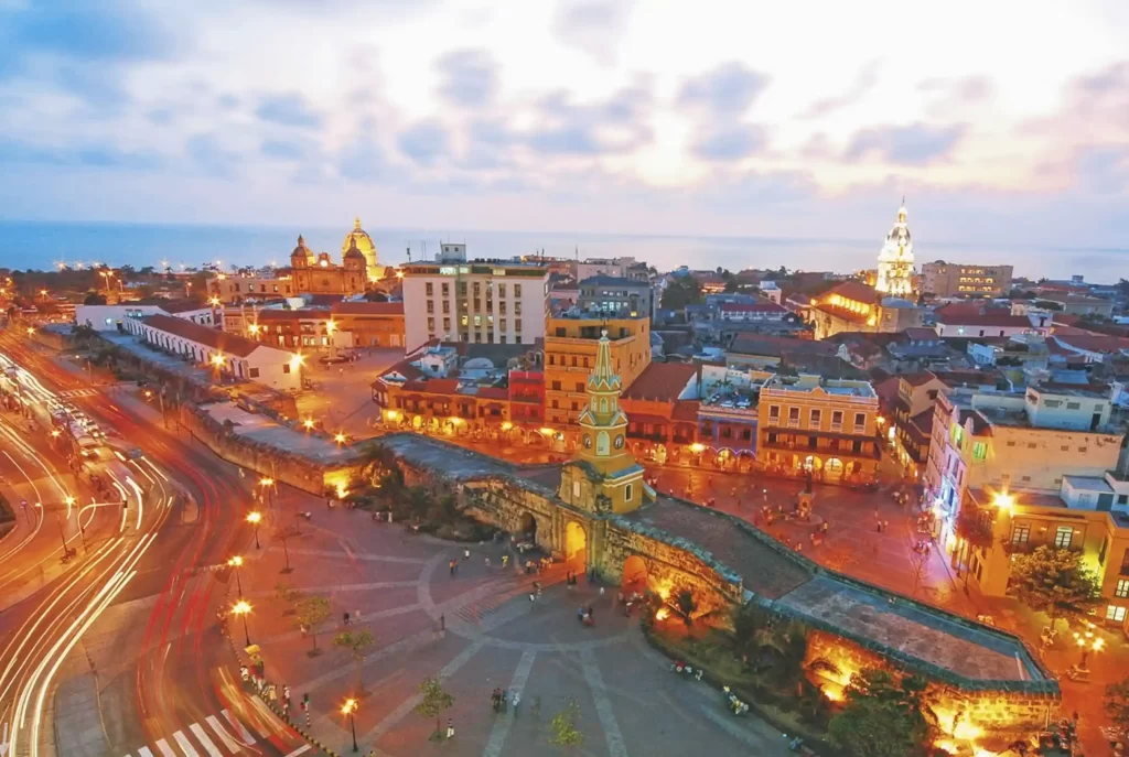 Aerial night view of Cartagena's historic center with the illuminated Clock Tower and colonial walls at dusk.