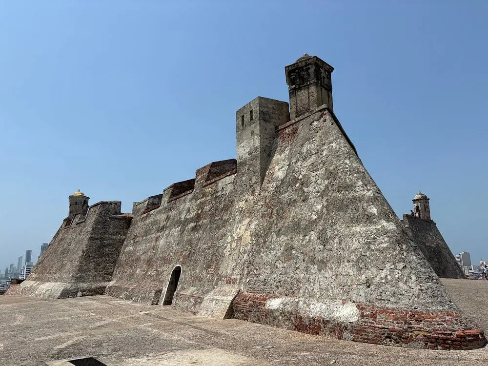 Murallas del Castillo San Felipe de Barajas en Cartagena con garitas coloniales y skyline de Bocagrande al fondo.