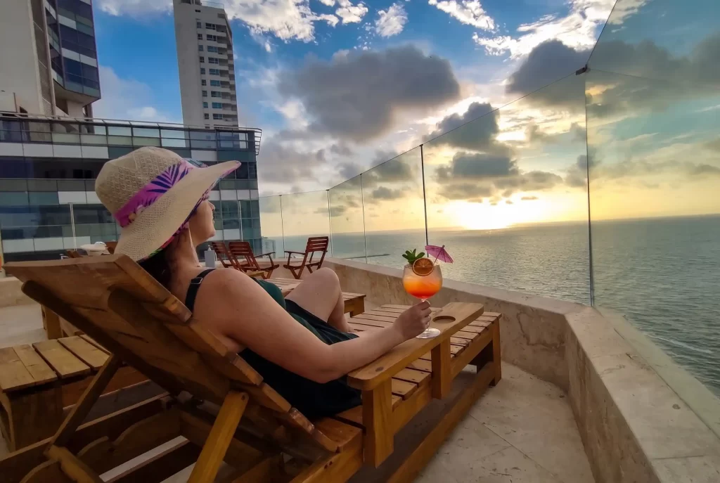 Mujer disfrutando cóctel en rooftop frente al mar Caribe al atardecer en hotel de Bocagrande, Cartagena.