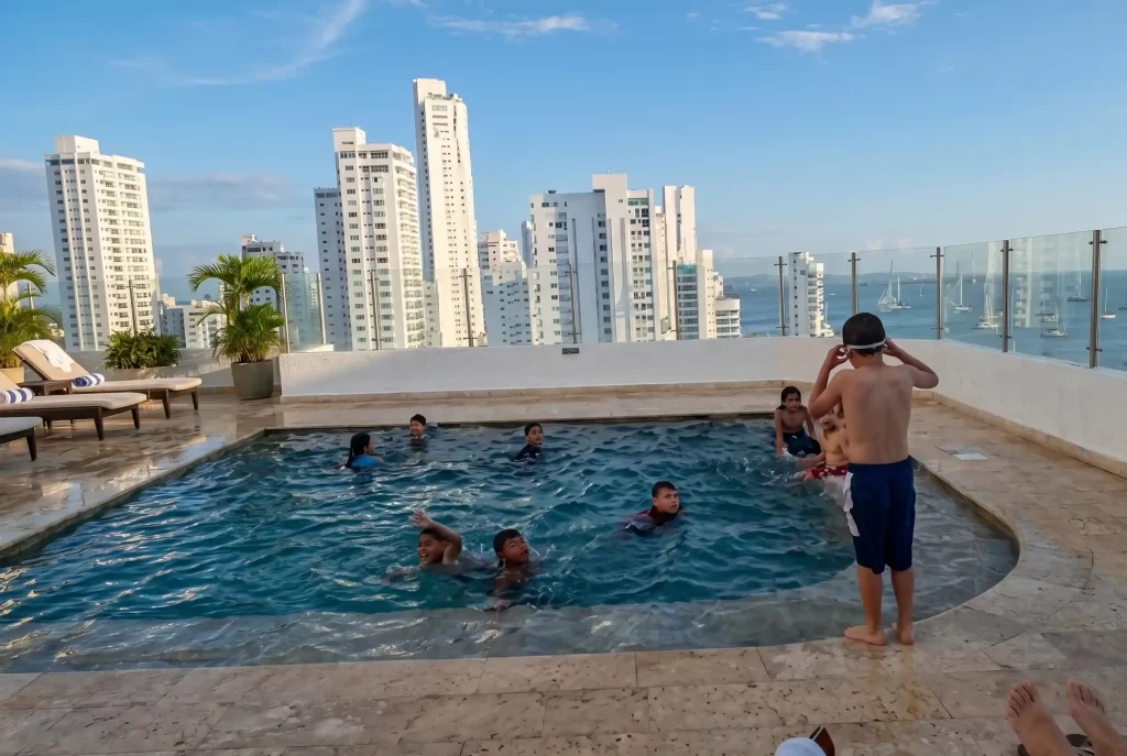 Children swimming in Hotel Regatta's rooftop pool with Bocagrande skyline and sailboats in the bay.