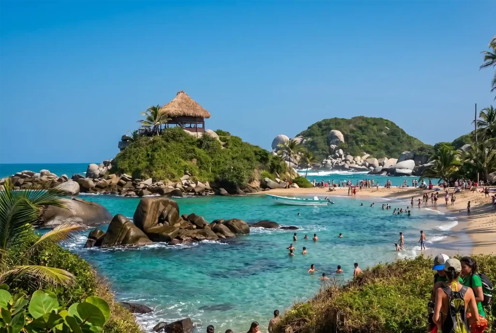 Playa del Parque Tayrona en Santa Marta con aguas turquesa, rocas y visitantes disfrutando el Caribe colombiano.