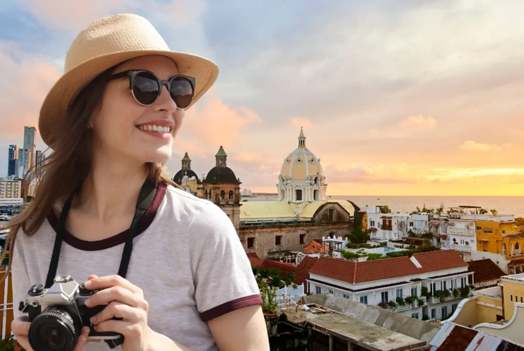 Tourist with hat, sunglasses and camera in front of Cartagena de Indias historic center at sunset.