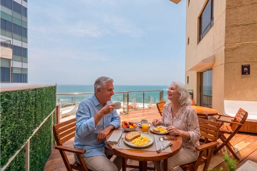 Pareja de adultos mayores desayunando en terraza con vista al mar
