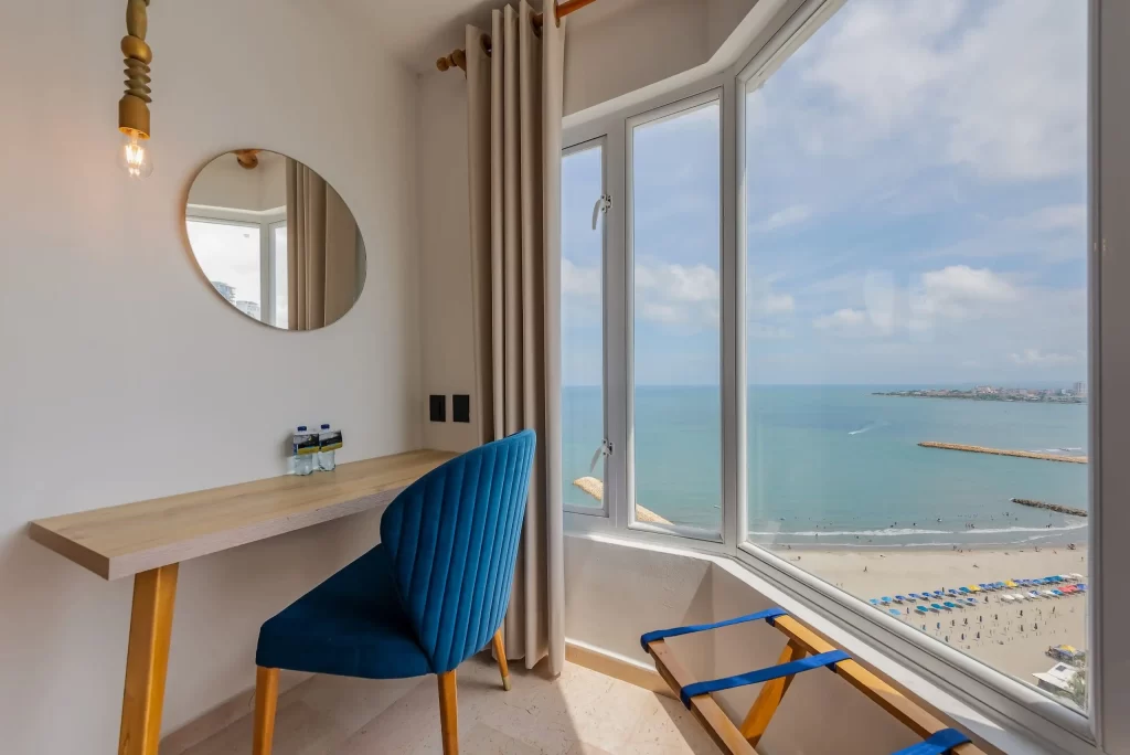 Work desk with a blue chair next to a large window with panoramic ocean views in a deluxe room at Hotel Regatta Cartagena.