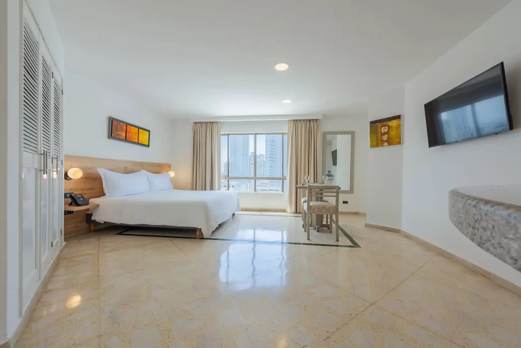 Amplia habitación estándar en el Hotel Regatta Cartagena con cama doble, mesa auxiliar, televisión y gran ventanal con vista a los edificios.