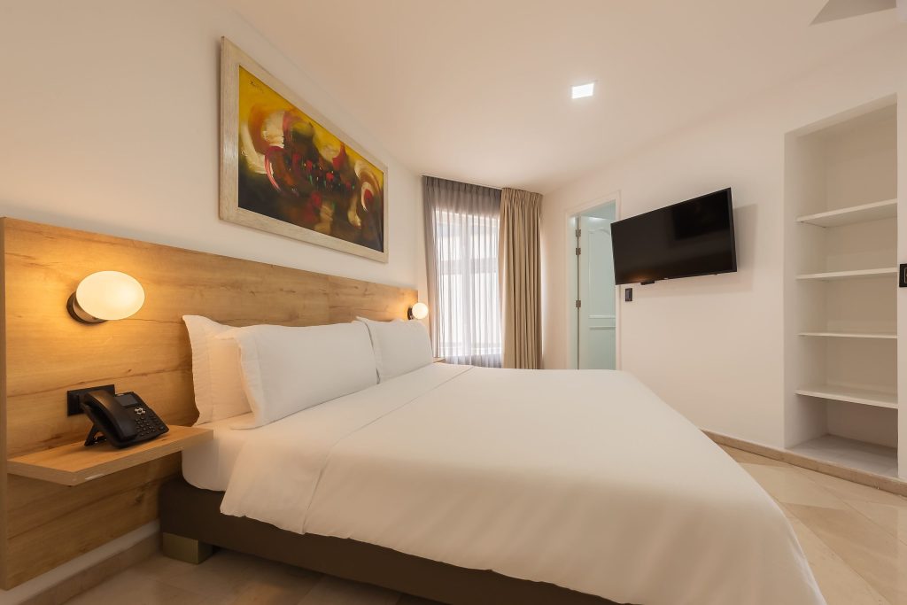 Habitación suite moderna en el Hotel Regatta Cartagena con cama matrimonial, iluminación cálida y televisión de pantalla plana.