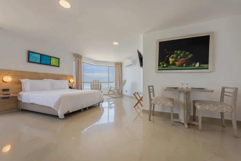 Amplia habitación superior en el Hotel Regatta Cartagena con cama doble, comedor, mecedoras junto a la ventana y vista al mar.