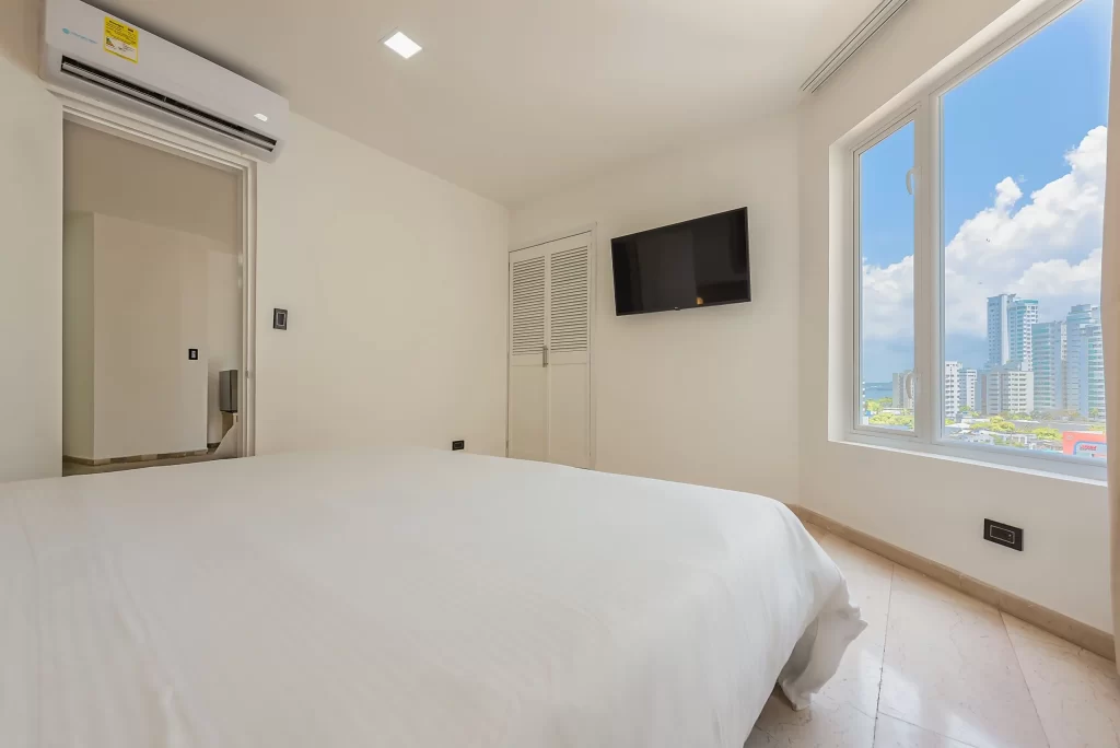 Bed in a junior suite room with air conditioning, wall-mounted TV, and large window with city views at Hotel Regatta Cartagena.