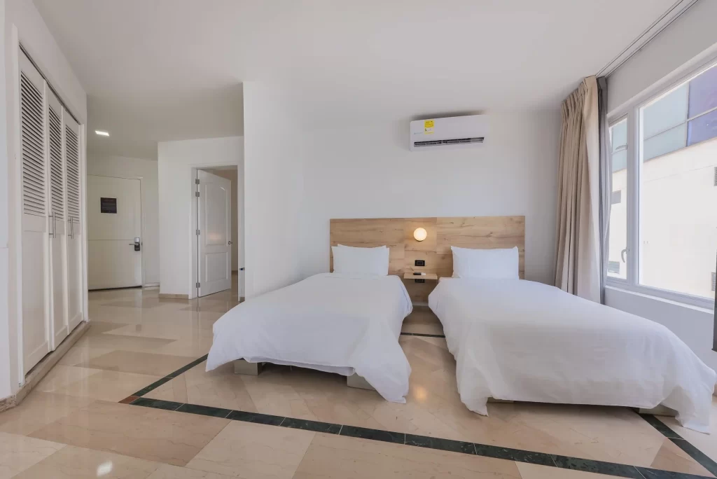 Amplia suite del Hotel Regatta Cartagena con dos camas sencillas, aire acondicionado y ventanal luminoso, ideal para grupos de hasta cinco personas.