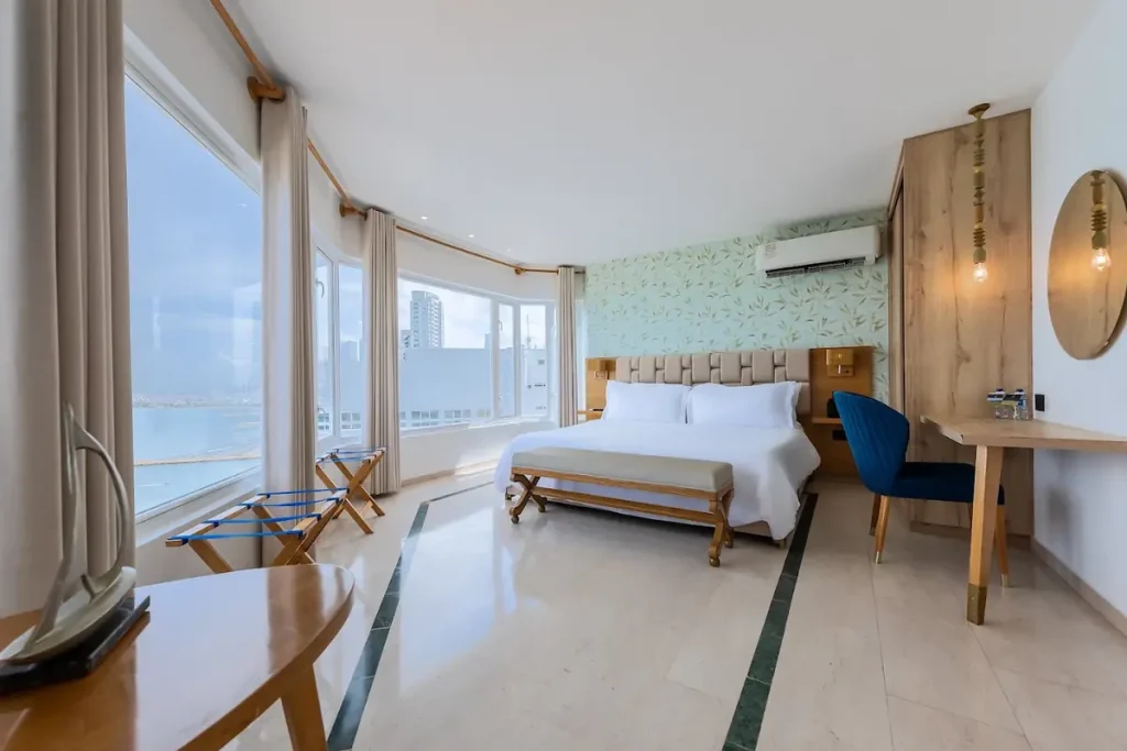 Habitación de hotel Regatta con cama matrimonial, zona de trabajo y ventanales panorámicos con vista al mar Caribe en Cartagena.