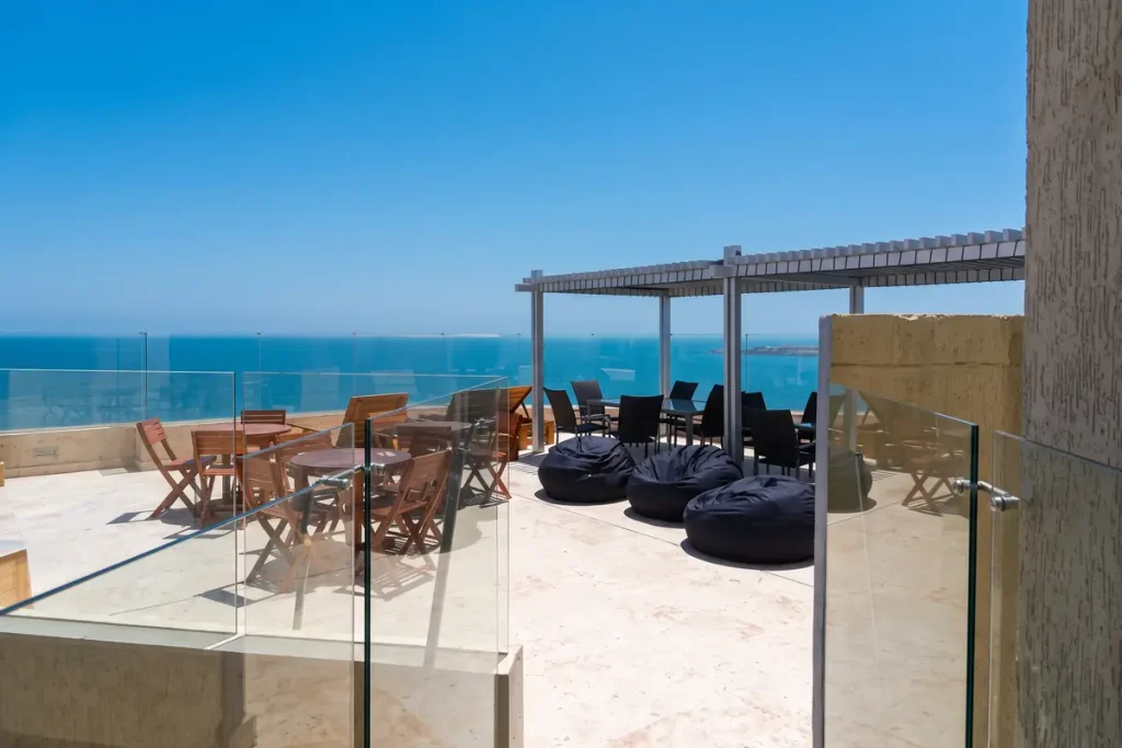 Terraza en la azotea de un hotel con mesas de madera, pufs y vista panorámica al mar Caribe.