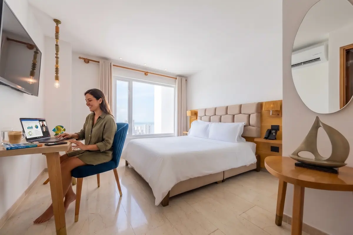 Mujer nómada digital trabajando con su computadora portátil en el escritorio de una habitación de hotel en Cartagena.