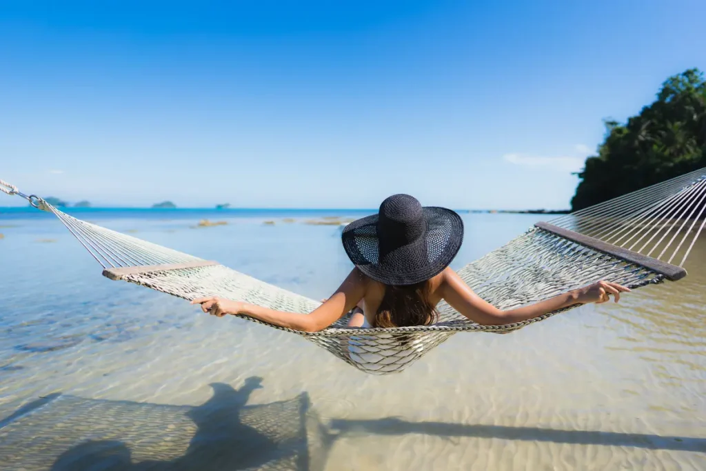 Mujer relajándose en una hamaca sobre aguas cristalinas durante un viaje slow en la playa.