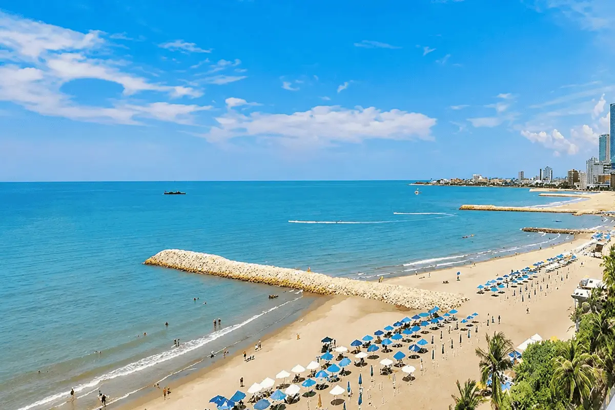 Vista aérea de la playa de Bocagrande con sombrillas azules y escollera, ideal para planear tu visita.